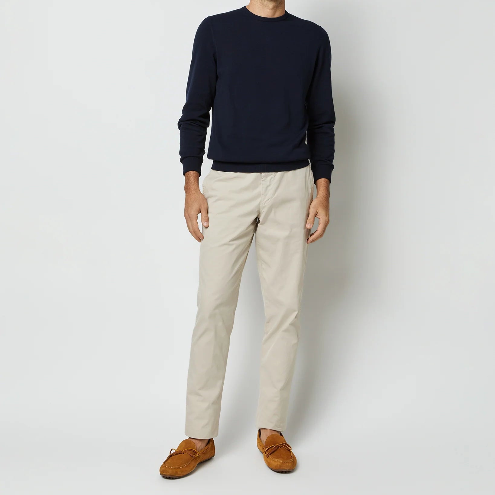A man, head out of frame, is seen against a plain background wearing a Sid Mashburn Crewneck Sweater in navy blue Egyptian cotton, paired with beige pants and brown loafers.