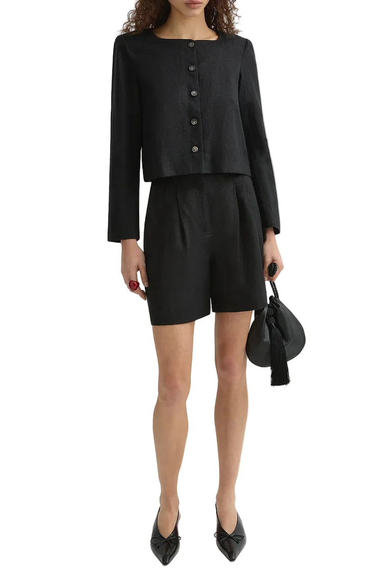 A woman wears the POSSE Marchello Short with a matching black button-up long-sleeve jacket, holding a black handbag and pairing the look with black pointed shoes.