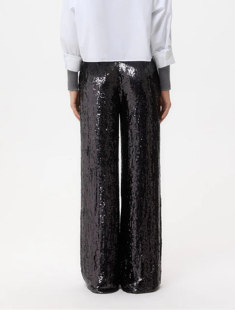 A person is seen from the back, wearing a white shirt and TWP's Adieu for Now Sequin Pant in black, against a plain background.