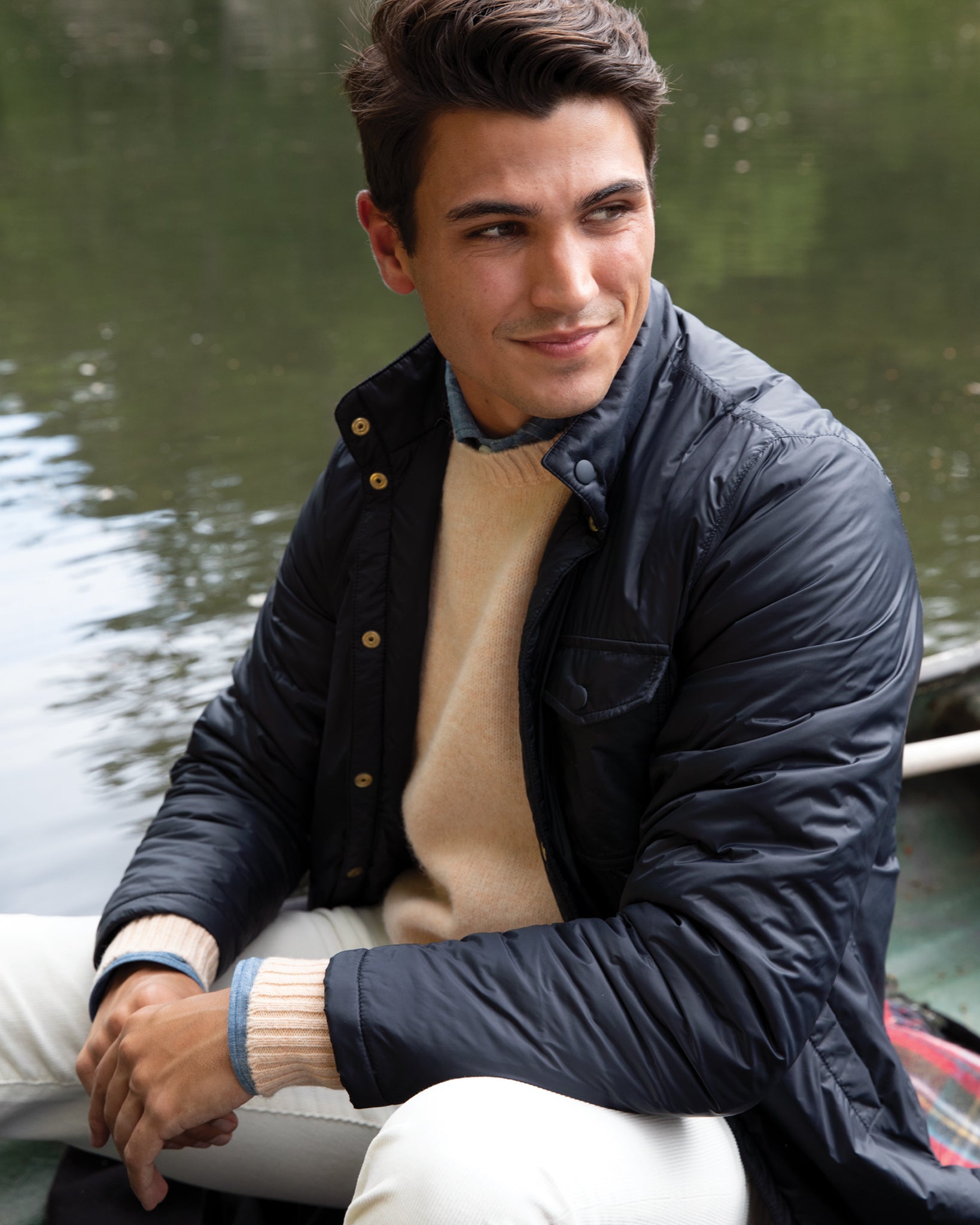 Man smiling while sitting in a boat, wearing a Sid Mashburn Cashpad Traveler's Jacket and recycled cashmere sweater.