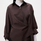 A person wears the TWP New Earl Shirt in dark brown, styled asymmetrically over a white turtleneck, pictured from shoulders to hips against a plain background.