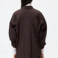 A person with long dark hair is shown from the back against a plain white background, wearing the TWP New Earl Shirt in dark brown over a white turtleneck and black pants.