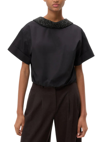 A person wearing the TWP Forever and Always Crystal Collar Shirt with short sleeves and dark high-waisted pants stands against a plain background.