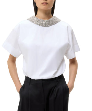 A woman wears the TWP Forever and Always Crystal Collar Shirt in white with short sleeves and black pants, standing with her hands in her pockets.