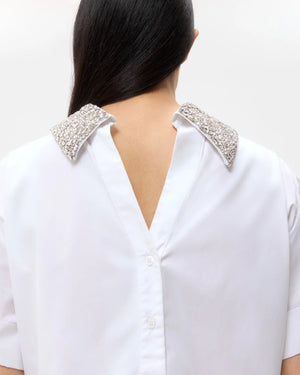 A person with long dark hair wears the TWP Forever and Always Crystal Collar Shirt, featuring an open back and crystal-embellished collar tips.