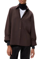 A person wears TWP's Next Morning Shirt, an oversized Italian cotton button down, over a white T-shirt and black turtleneck with black pants, creating a relaxed silhouette.