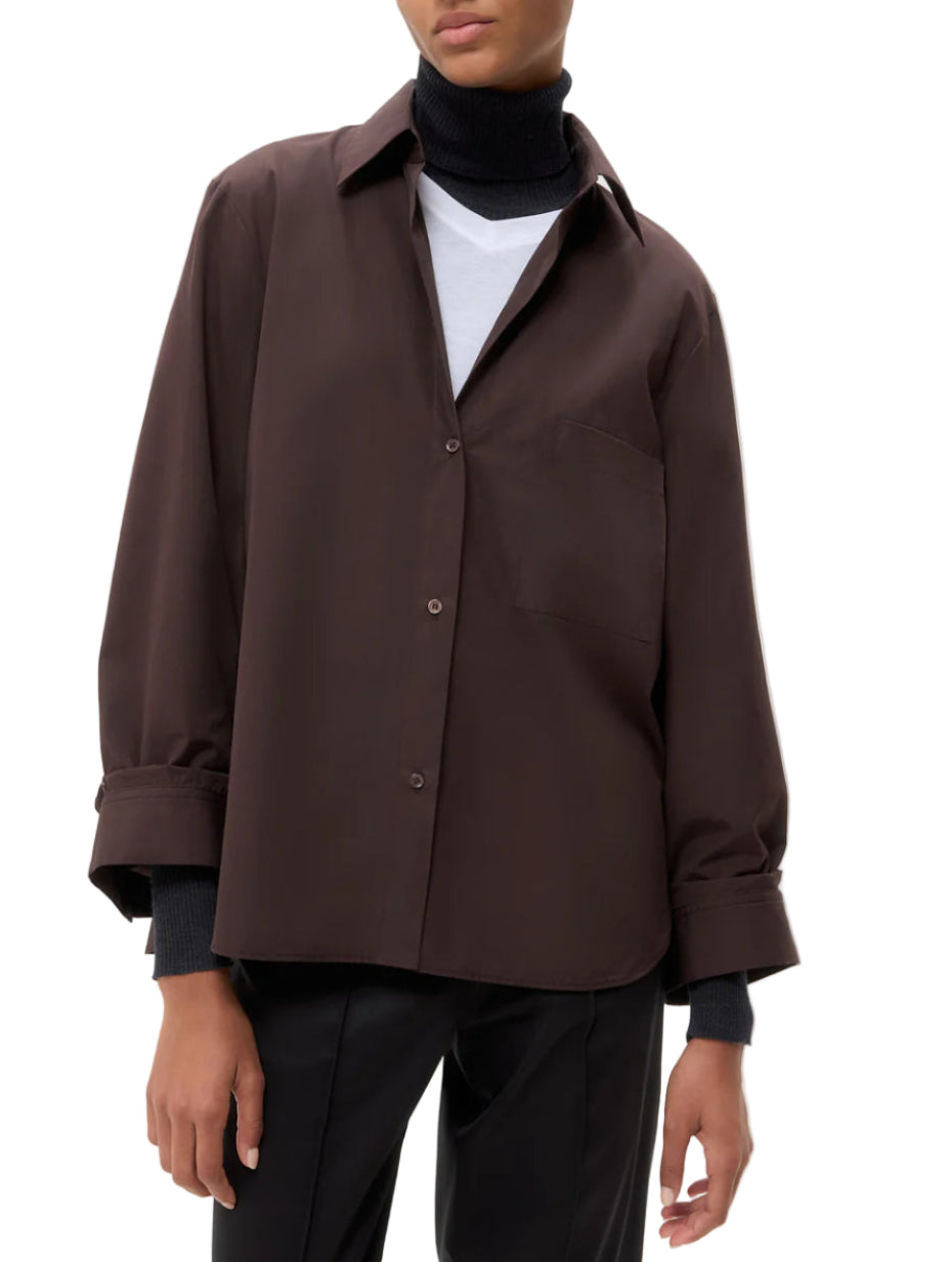 A person wears TWP's Next Morning Shirt, an oversized Italian cotton button down, over a white T-shirt and black turtleneck with black pants, creating a relaxed silhouette.
