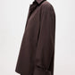 A person wears the TWP Next Morning Shirt, an oversized dark brown button-down with a chest pocket and relaxed fit, layered over a black turtleneck against a plain light background.