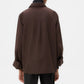 A person is seen from behind wearing the TWP Next Morning Shirt—an oversized brown Italian cotton button down with a relaxed fit and buttoned cuffs—set against a plain white background.