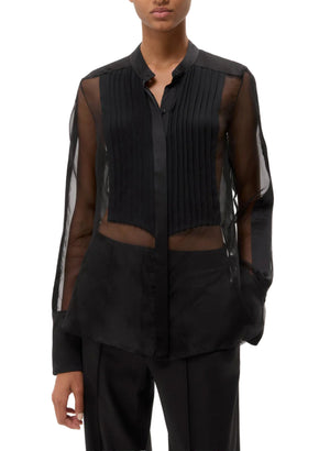 A person wears the TWP Peyton Silk Organza Shirt, styled oversized with pleated front detailing, paired with black pants; their face is partially out of frame.