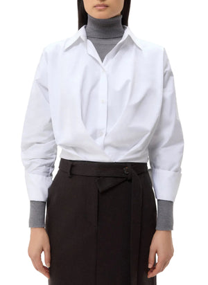 A person wears the oversized TWP Taken Shirt over a gray turtleneck sweater, paired with high-waisted black pants with a tie belt.
