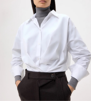 A person wears the TWP Taken Shirt over a gray turtleneck sweater with high-waisted dark trousers; their face is partially out of frame.