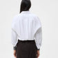 A person stands with their back to the camera, wearing the oversized cropped Taken Shirt by TWP and a black skirt against a plain light background.
