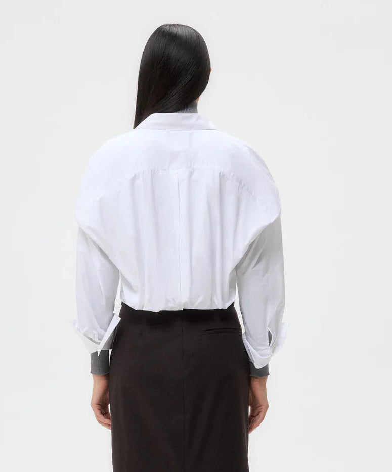 A person stands with their back to the camera, wearing the oversized cropped Taken Shirt by TWP and a black skirt against a plain light background.