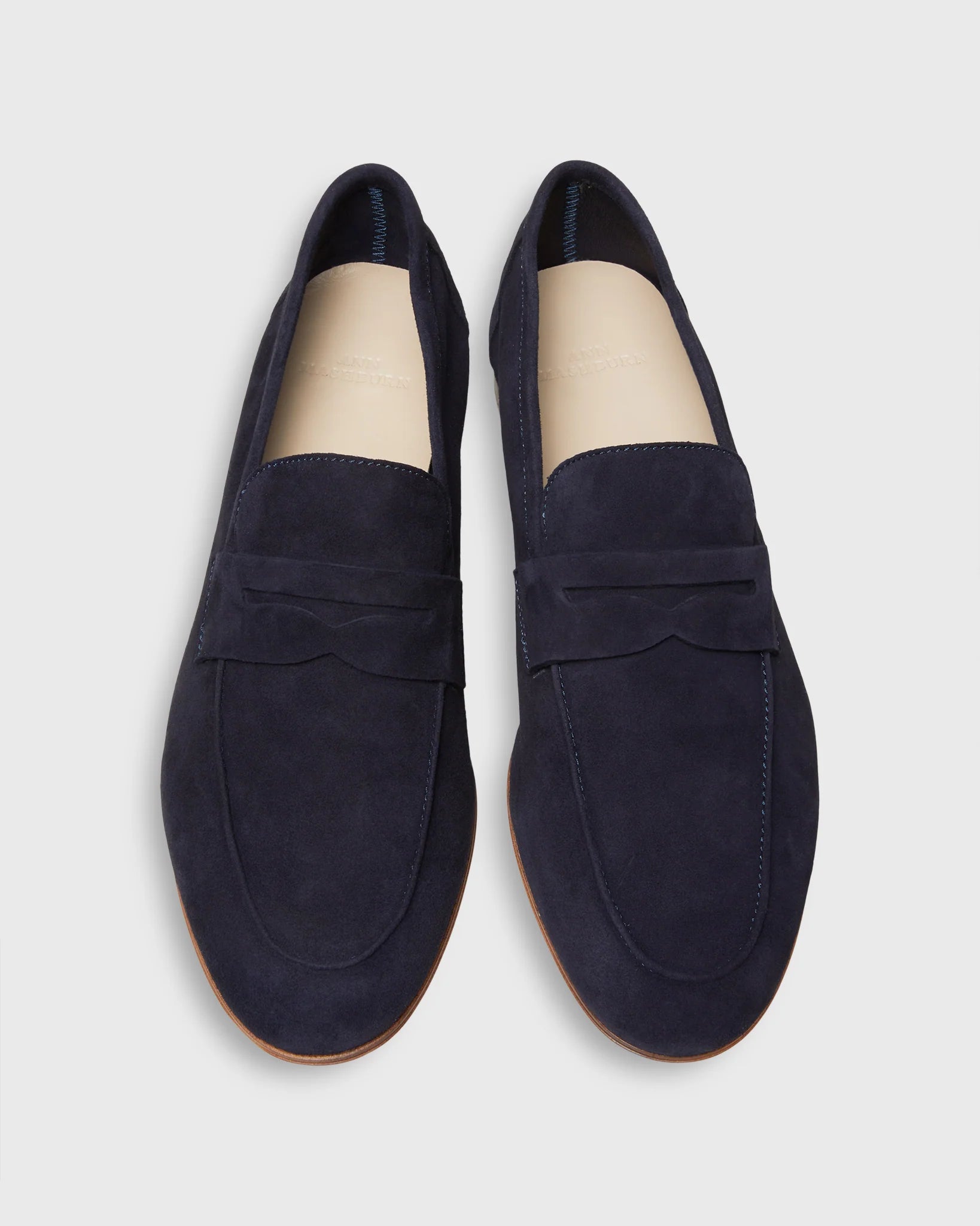 The Ann Mashburn Mia Suede Loafer: navy blue Italian suede loafers with tan insoles and light brown soles—an elevated staple for any menswear collection, shown from above on a plain background.