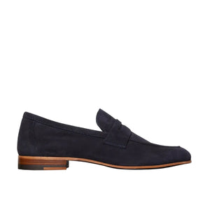 The Ann Mashburn Mia Suede Loafer is a navy blue Italian shoe with a rounded toe and low wooden heel, shown in side profile against a white background.