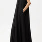 A woman stands sideways against a plain white background wearing the TWP Capitol Crystal Collar Dress, a sleeveless, floor-length black gown with an A-line silhouette and pockets.