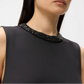 A woman wears the TWP Capitol Crystal Collar Dress, featuring a sleeveless black design and a high crystal collar, shown from the shoulders up against a plain background.