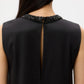 A close-up of a person wearing the TWP Capitol Crystal Collar Dress, a sleeveless black dress featuring a beaded neckline, crystal collar, and keyhole opening at the back.