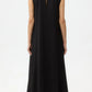 A person stands facing away, wearing the TWP Capitol Crystal Collar Dress—a long, sleeveless silk-finish gown with an A-line silhouette, high neckline, and small back keyhole—set against a plain white background.