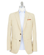 Sid Mashburn's Butcher Jacket, crafted from a refined cotton and canapa blend in beige, features two dark buttons and three front pockets inspired by a classic chore coat, and is shown paired with a light blue striped dress shirt on a mannequin.