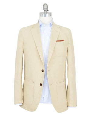 Sid Mashburn's Butcher Jacket, crafted from a refined cotton and canapa blend in beige, features two dark buttons and three front pockets inspired by a classic chore coat, and is shown paired with a light blue striped dress shirt on a mannequin.