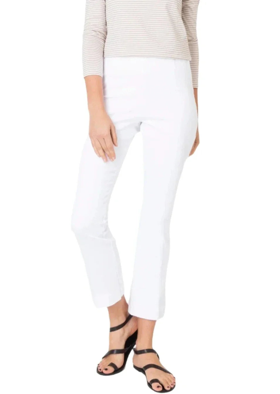 A person wearing a beige long-sleeve top, Ann Mashburn Faye Flare Cropped Stretch Twill Pant, and black sandals is standing against a white background.