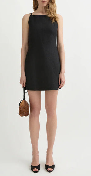 A woman poses against a plain background wearing the POSSE Neve Mini Dress, featuring a square neckline. She holds a small brown purse and pairs the look with black open-toe heels.