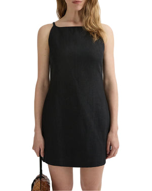 A woman holds a small brown bag by her side, wearing the POSSE Neve Mini Dress—a sleeveless, knee-length black dress—against a plain white background for an effortlessly elegant look.