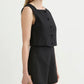 A woman wears the POSSE Rio Top, a sleeveless black buttoned crop top with a high neckline, paired with matching black high-waisted shorts and holds a small beaded handbag.