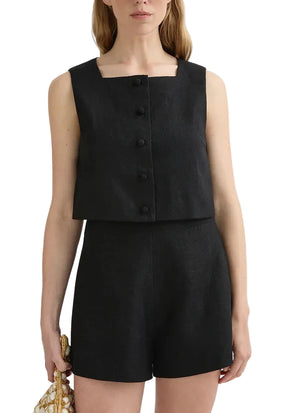 A woman wears the POSSE Rio Top—a black, sleeveless, square-neck button-front top—paired with matching high-waisted mid-weight linen shorts and holds a textured bag in one hand.