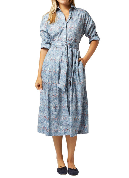 A woman wearing a blue floral midi Ann Mashburn Kimono shirtwaist dress with a tie waist and navy blue flats.