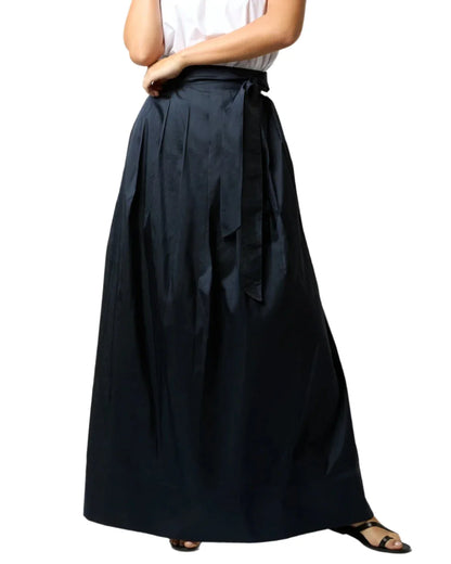 A person is wearing the Ann Mashburn Silk Shantung Pleated Wrap Skirt, paired with a white shirt and black sandals.