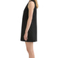 A woman stands in profile against a white background, wearing the POSSE Nancy Mini Dress—a sleeveless black linen piece featuring an A-line silhouette.