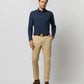 A man stands against a plain background wearing a Sid Mashburn Long-Sleeve Polo in navy, beige chinos, a brown belt, and brown shoes.