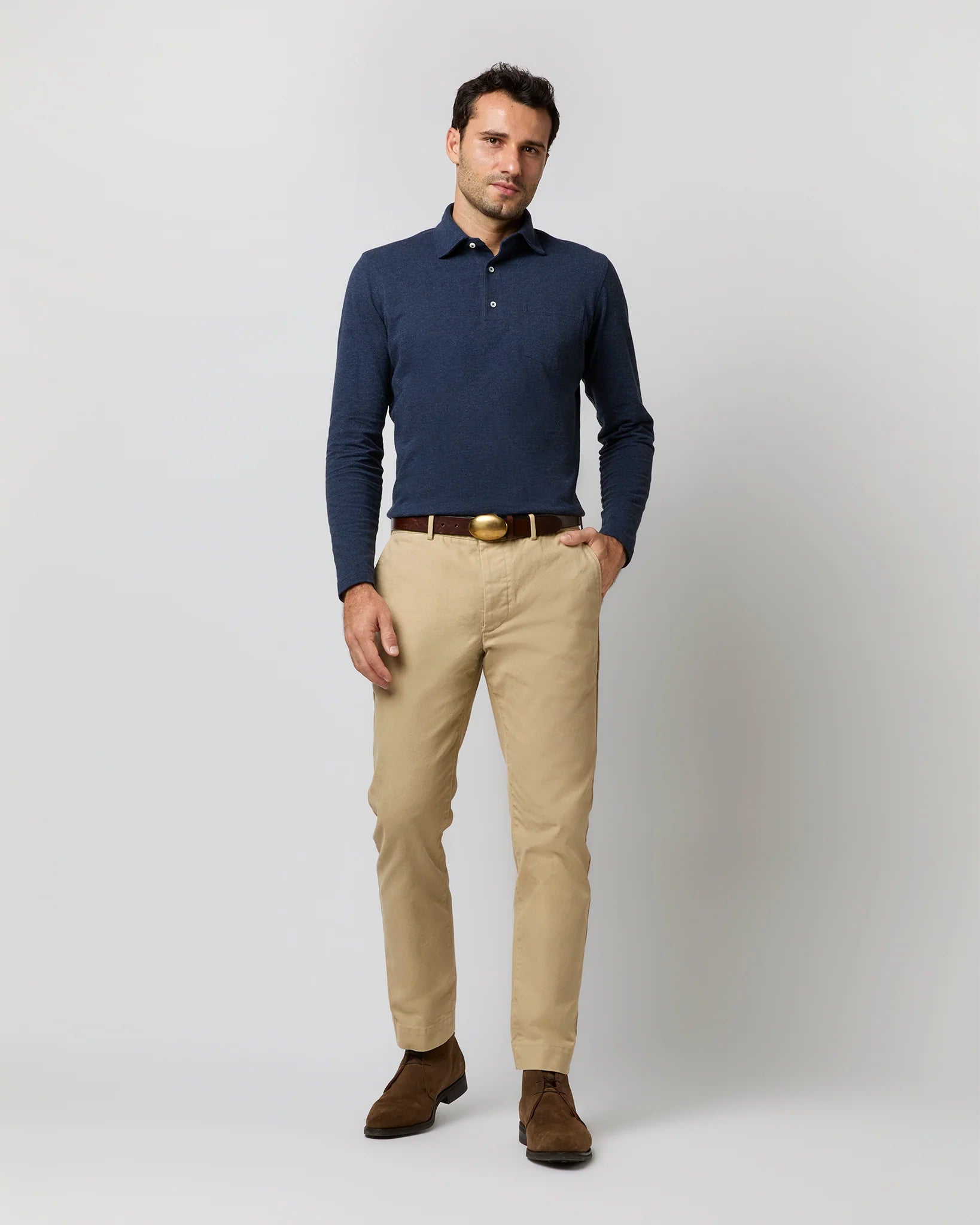 A man stands against a plain background wearing a Sid Mashburn Long-Sleeve Polo in navy, beige chinos, a brown belt, and brown shoes.