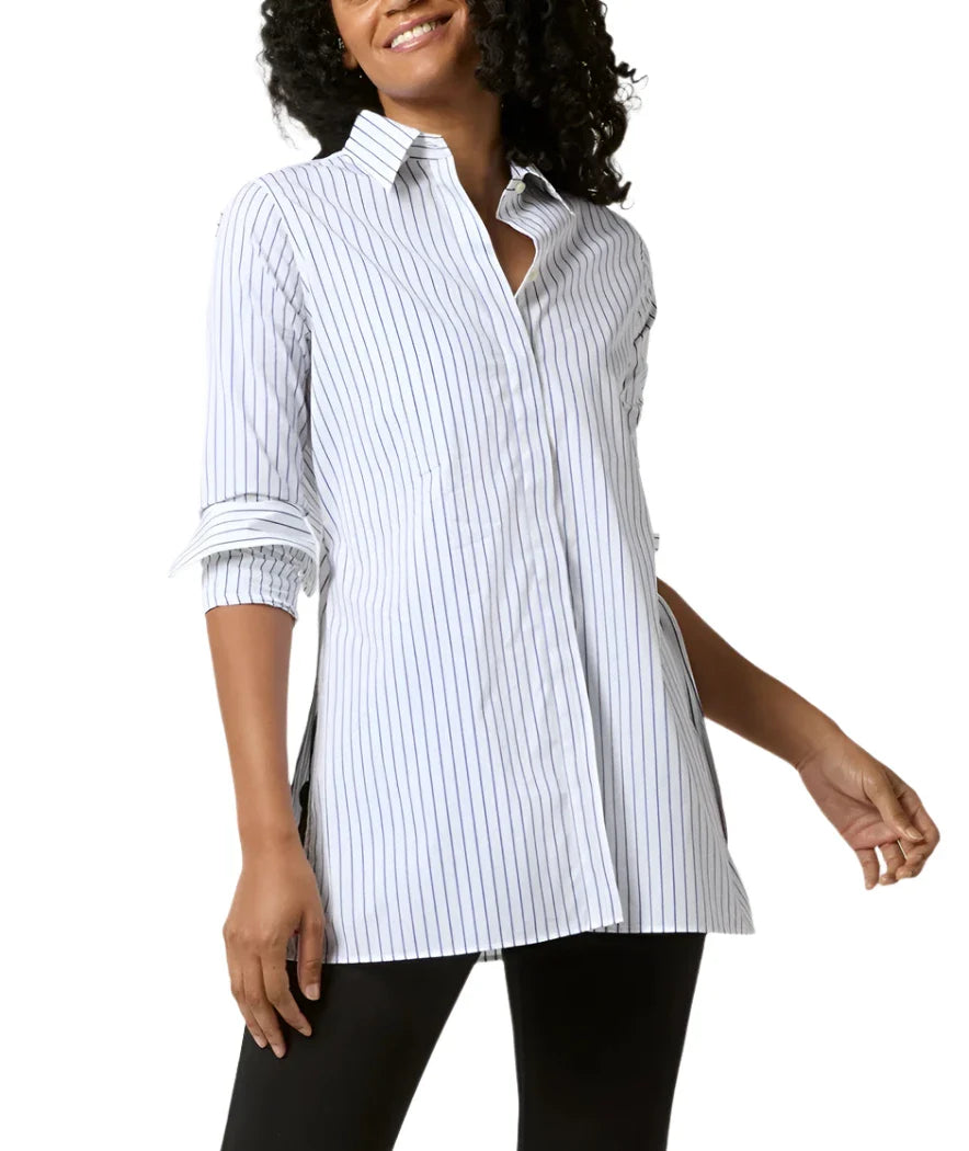 A person wearing the Ann Mashburn Gabrielle Tie Tunic, a white, long-sleeve, button-up shirt made of 100% cotton Italian poplin with vertical stripes from the brand Ann Mashburn, stands in a casual pose.