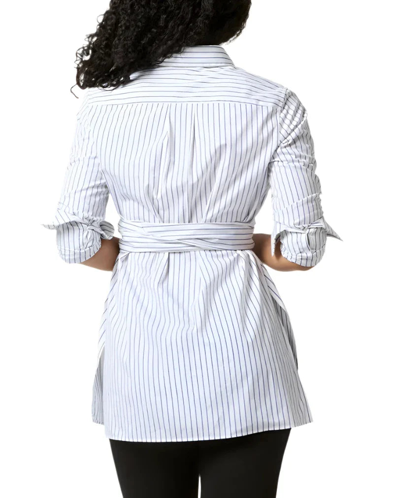 A woman is seen from behind wearing the Ann Mashburn Gabrielle Tie Tunic, a white, long-sleeve, striped shirt made of Italian poplin with sleeves rolled up and a tied waist, paired with black pants.