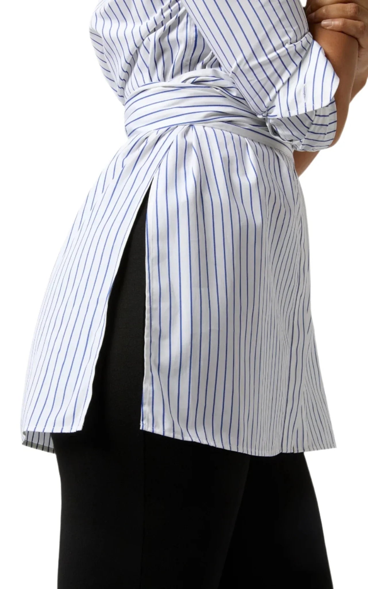 A side view of a person wearing the Ann Mashburn Gabrielle Tie Tunic, a white, striped, long-sleeved tunic with a split-side design and a belt, crafted from 100% cotton Italian poplin, paired with black pants.