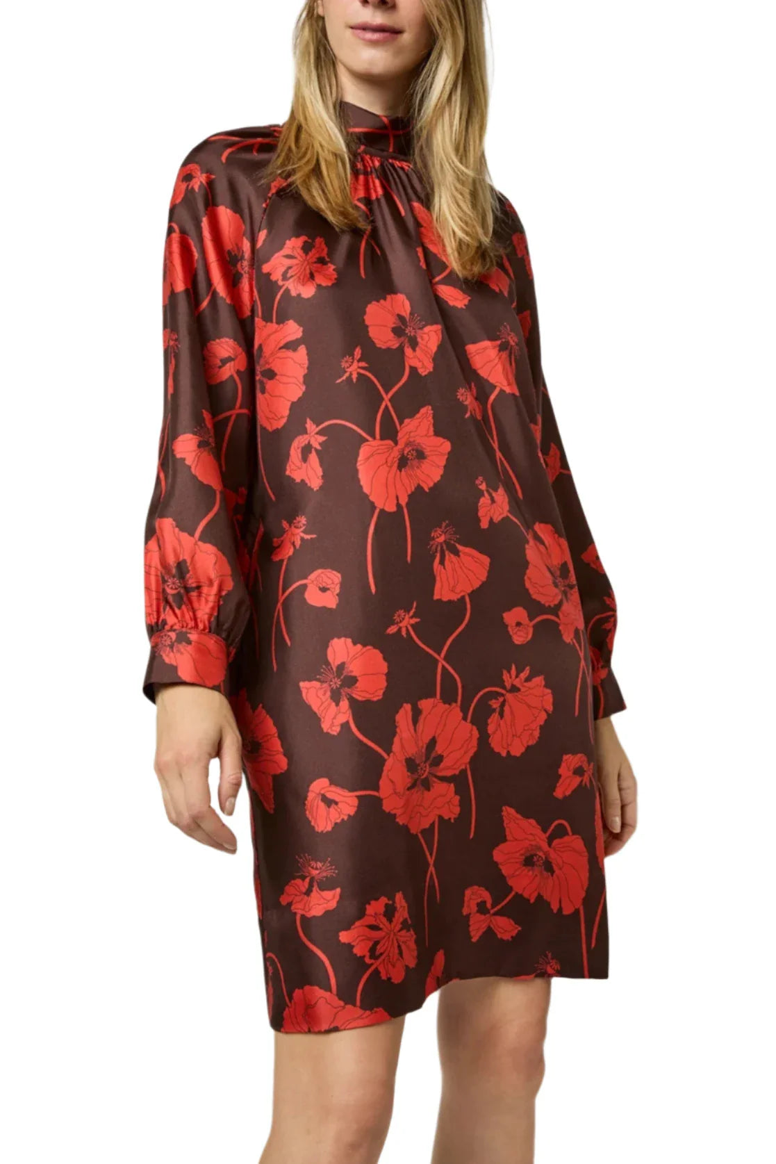 A woman is wearing the Ann Mashburn Maggie Dress, a knee-length autumn dress with a red floral pattern and long sleeves, crafted from luxurious brown silk twill.