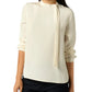 A woman wearing the Pippa Top by Ann Mashburn, a cream crepe de chine blouse with an asymmetrical tie detail, paired with black pants.