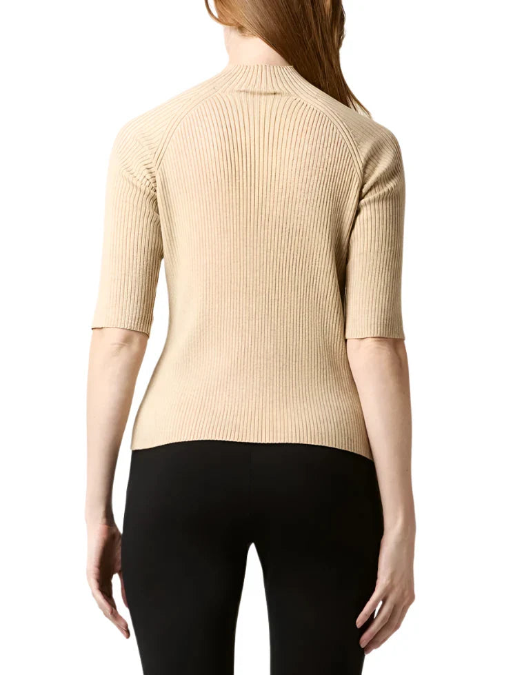 A person with long brown hair is shown from the back, wearing the Ann Mashburn Mackenzie Sweater in beige ribbed fabric with elbow-length sleeves, paired with black pants.