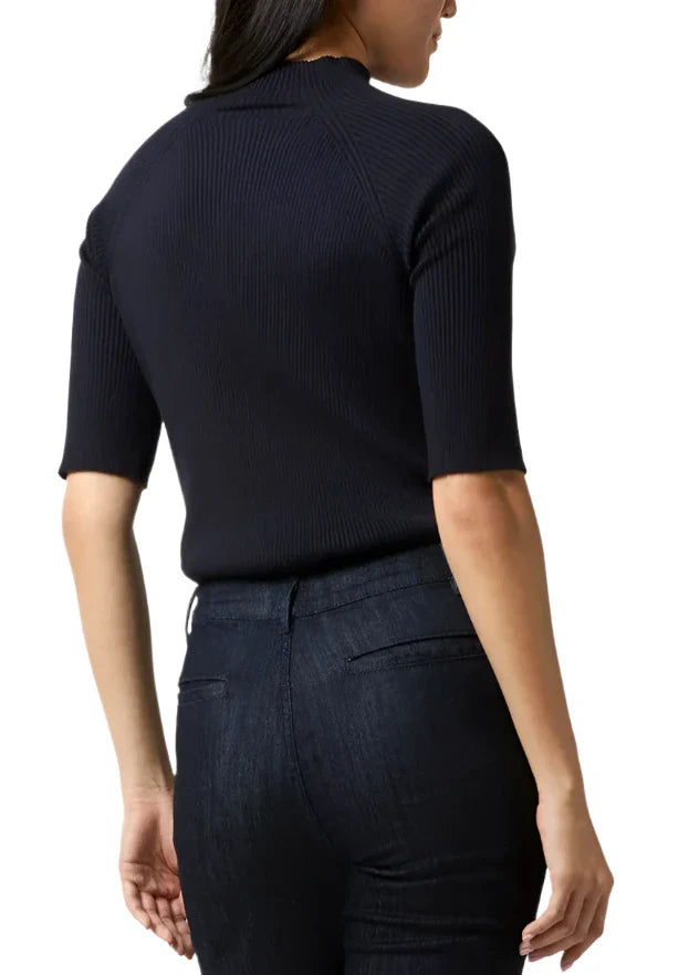 Mackenzie is shown from the back, wearing the Ann Mashburn Mackenzie Sweater, a short-sleeve black stretchy top, paired with dark jeans, standing against a plain white background.