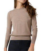 A person wearing an Ann Mashburn Alida Crewneck Sweater, a fine-gauge, light brown, long-sleeved top paired with black pants. The person has long, wavy hair and a neutral facial expression.