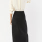A woman stands facing away, wearing the Ann Mashburn Long Pencil Silk Faille Skirt with a white silk long-sleeve blouse with rolled-up sleeves.