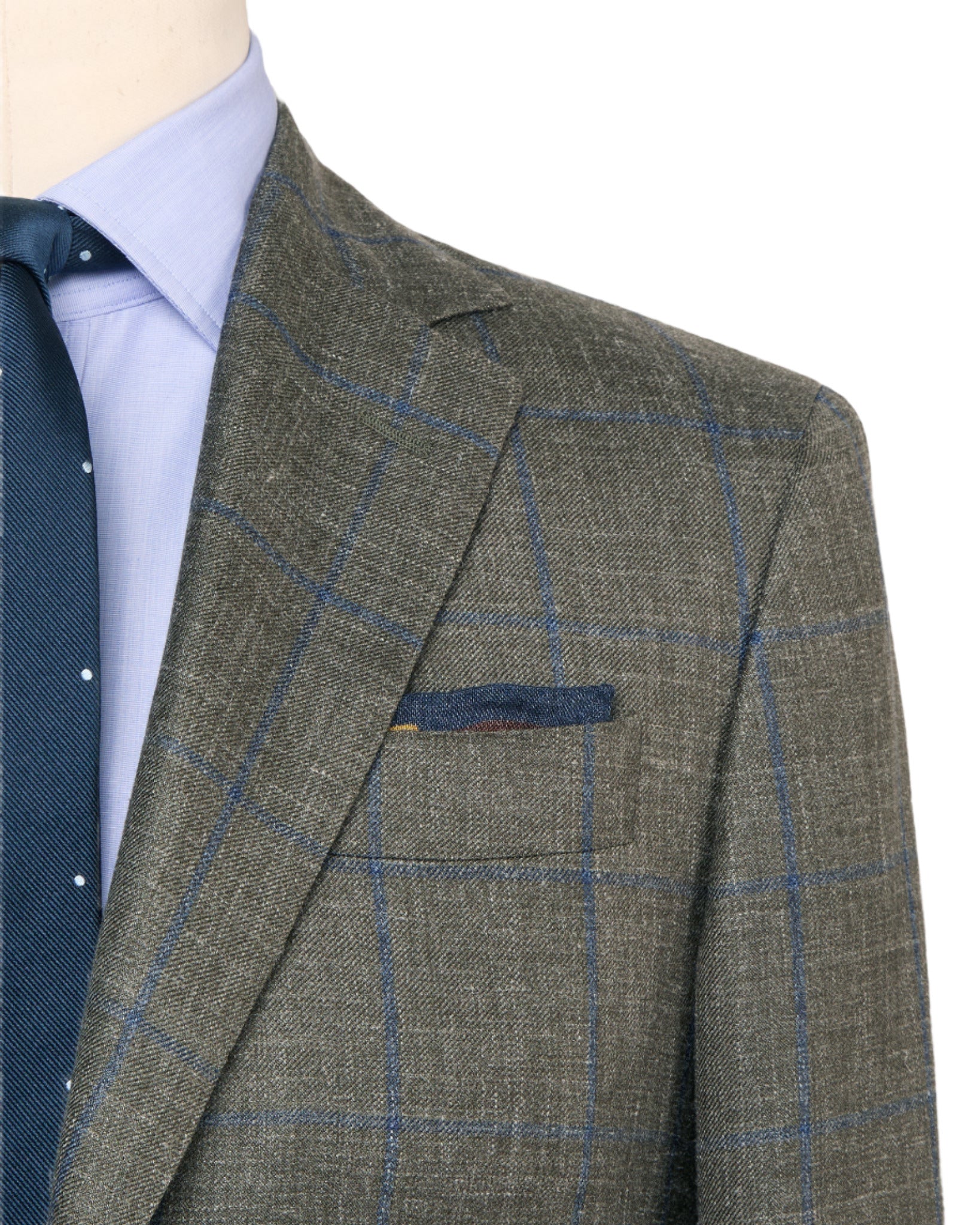 Close-up of a person wearing the Sid Mashburn Virgil No. 2 Jacket in grey plaid silk and linen, paired with a light blue dress shirt and a navy tie with small white dots.