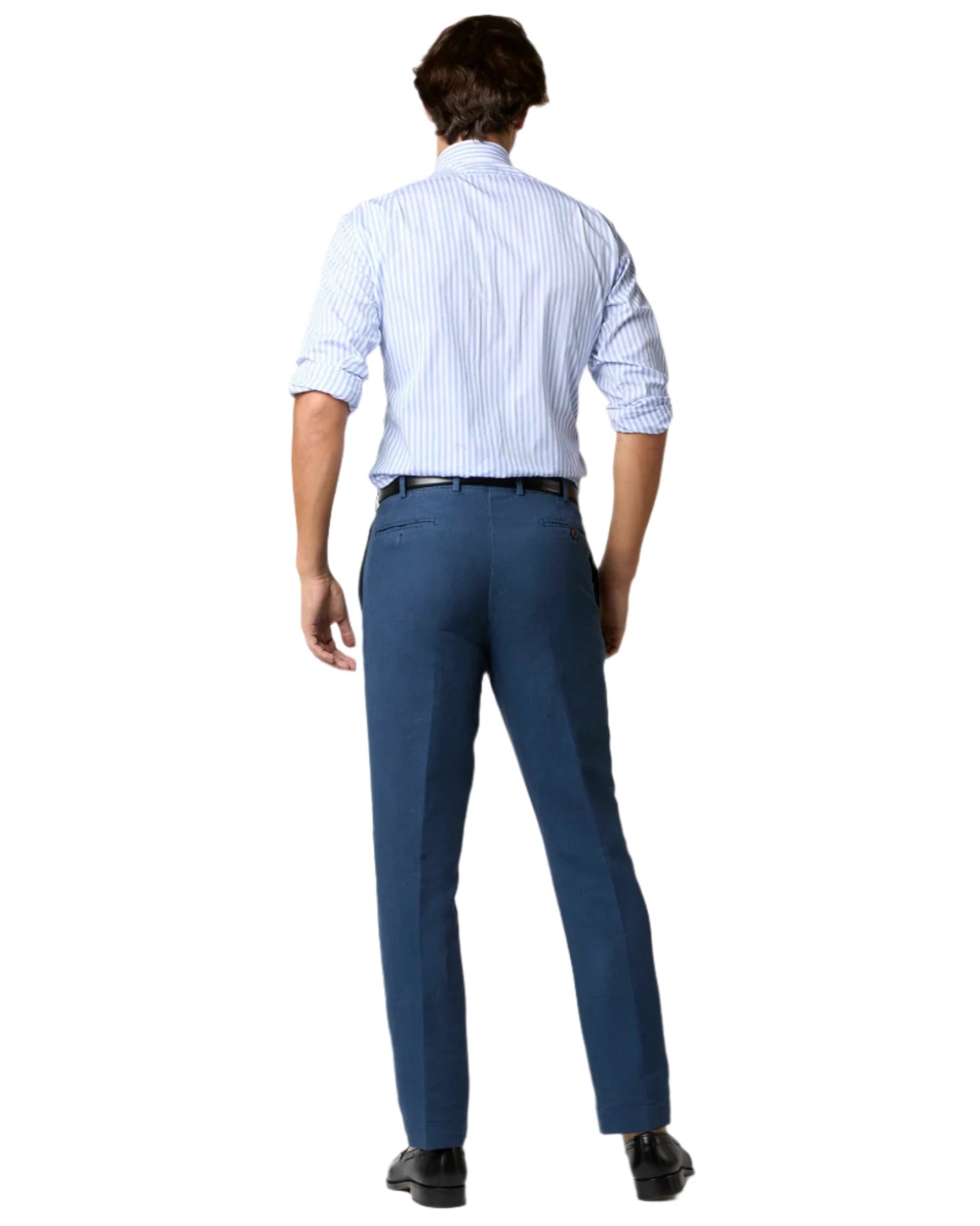 A man faces away, wearing a light blue striped shirt with rolled-up sleeves, Sid Mashburn Sport Trousers in Italian spun fabric, and black shoes, all set against a white background.