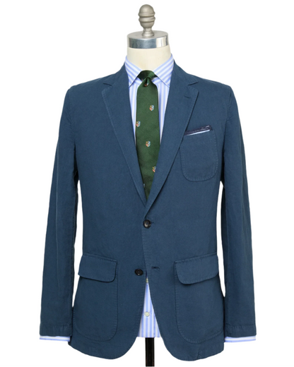The Sid Mashburn Butcher Jacket is showcased on a mannequin, paired with a blue and white striped shirt and a patterned green tie.