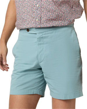A person is wearing Sid Mashburn Sport Shorts Side Tab in light blue seersucker with elasticized tabs, paired with a pink patterned button-up shirt; only the lower torso and upper legs are visible.