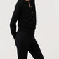 A person wears the Ann Mashburn Rosie Cotton Silk Cardigan in black with black pants, standing sideways against a plain light background, arms relaxed behind their back.